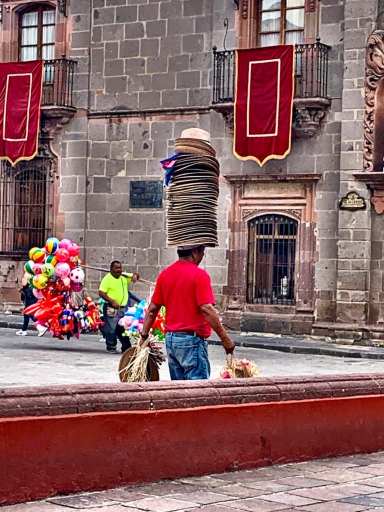 Vendor walking with hats piled on his head, another example of people watching for fun in SMA.