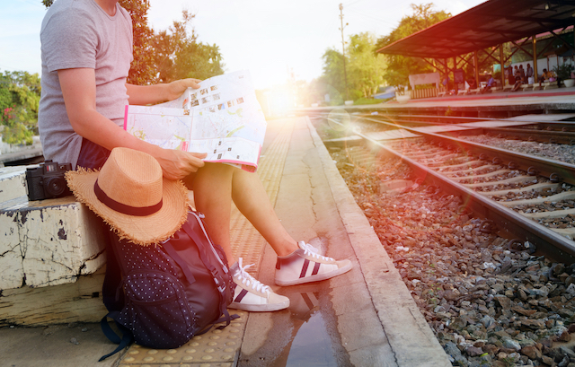 Man sitting on a bench at a train station with his belongings scattered around him does not have any anti-pickpocket travel gear.