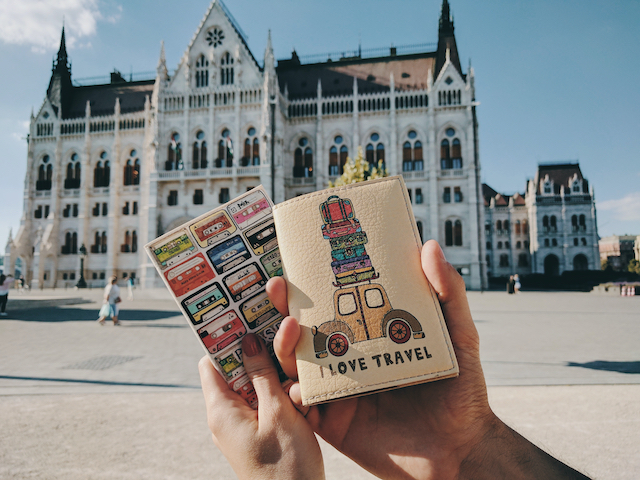 Person outside in front of a building holding a passport as they travel.