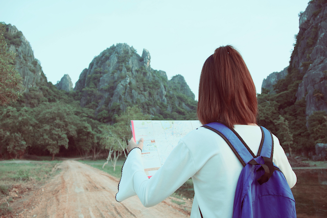 young girl with backpack enjoying sunset on peak mountain, looking a map  