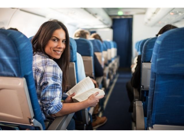 Woman reading a book on an airplane looking back at her companion.