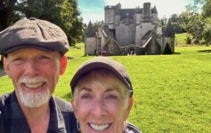 Two people wearing scottish type hats standing out in front of a castle