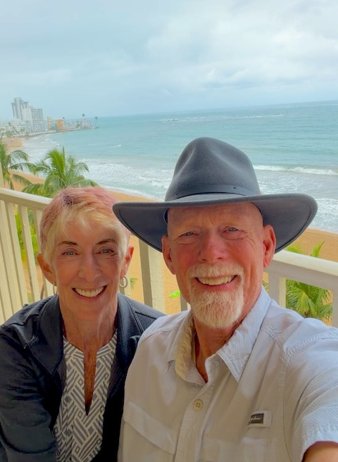Two people sitting on a balcony with the beach, palm trees and ocean behind them in the Marriott Stelaris in San Juan Puerto Rico